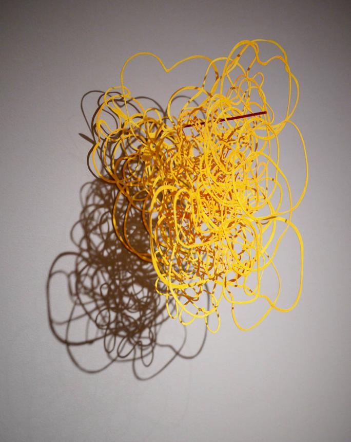 Individual view of a single wall mounted piece consisting of what looks like yellow tangled yarn
