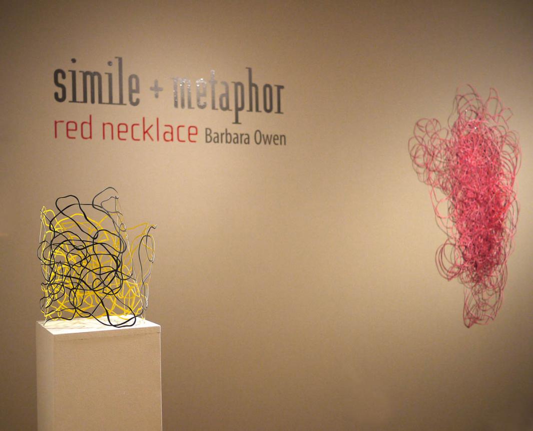 Gallery view of the entrance with show name on the wall, one wall piece, and one piece on a plinth
